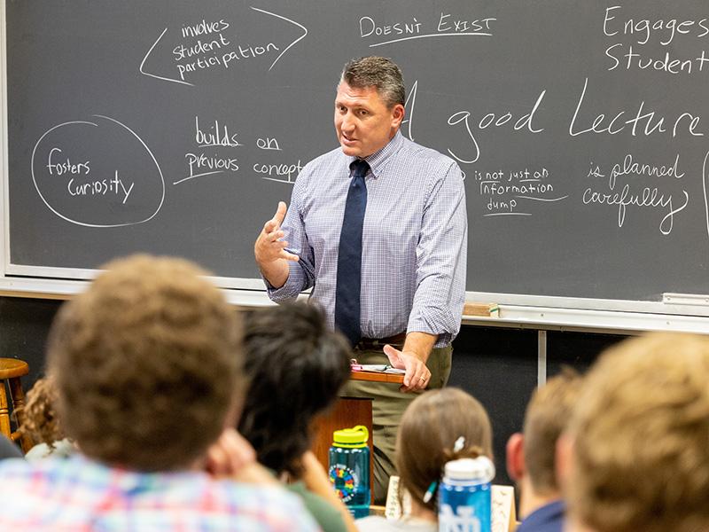 Professor stands in from of chalkboard filled with words to describe great leadership